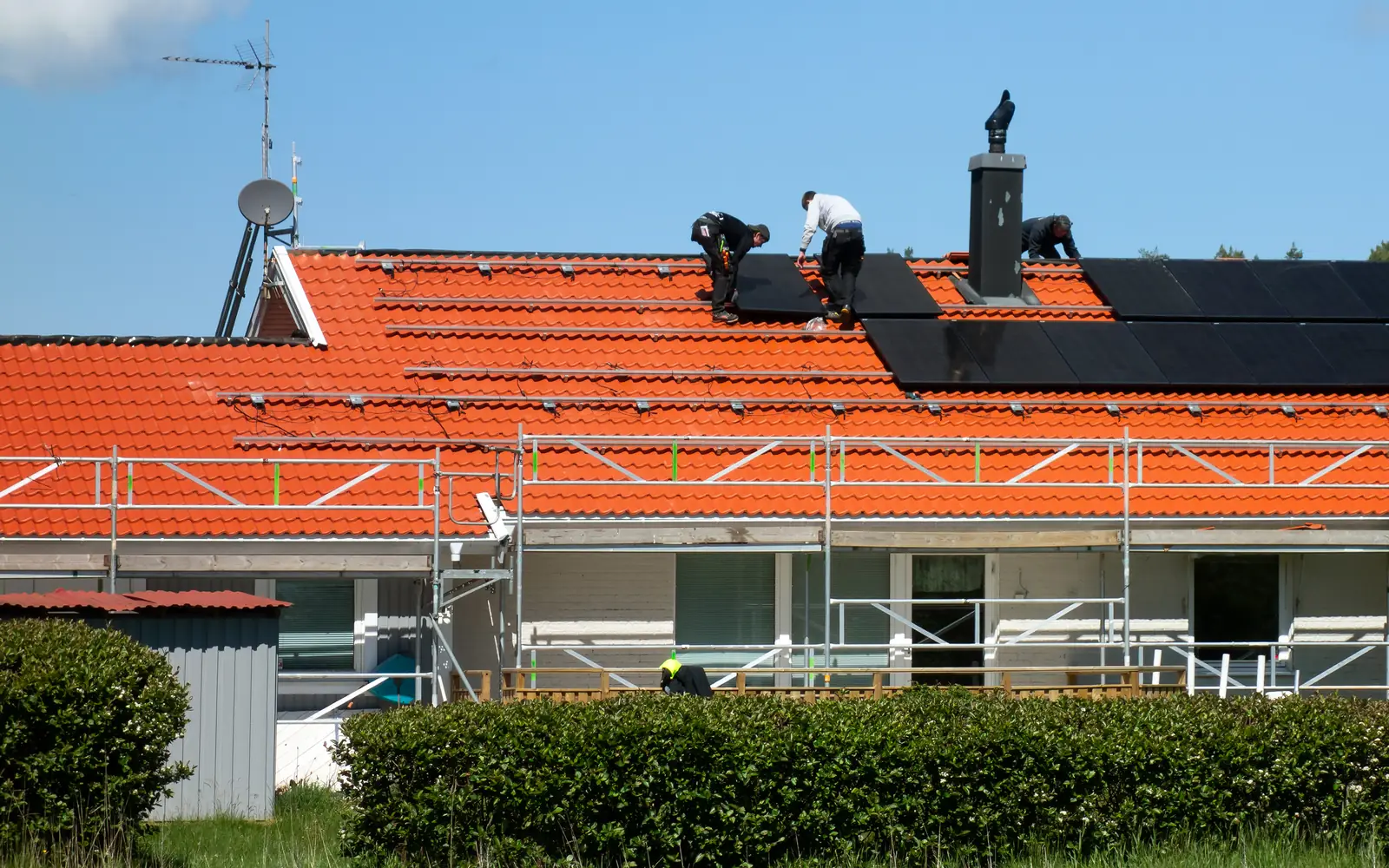 Monteure legen schwarze Solarmodule auf die Schienen eines roten Ziegeldachs, das Haus ist eingerüstet (Herne)