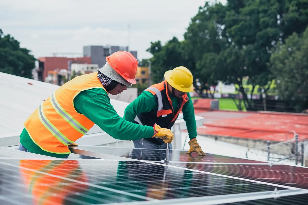 Zwei Monteure mit Schutzhelm und Warnweste richten ein Solarmodul auf einem Flachdach aus (Nahrendorf, Landkreis Lüneburg)