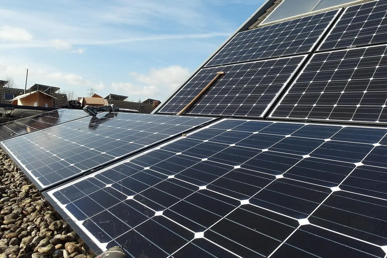Schräg aufgeständerte Solarmodule auf einem bekiesten Flachdach neben einer Dachfläche mit Modulen