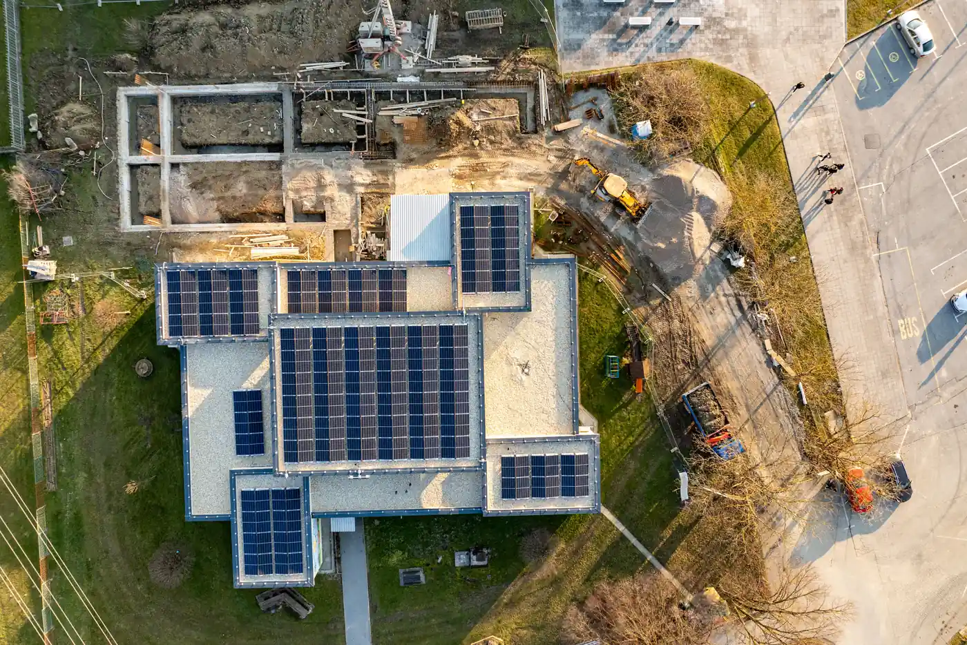 Luftbild eines neuen Hauses mit Solarmodulen auf mehreren Flachdachflächen, daneben eine Baustelle