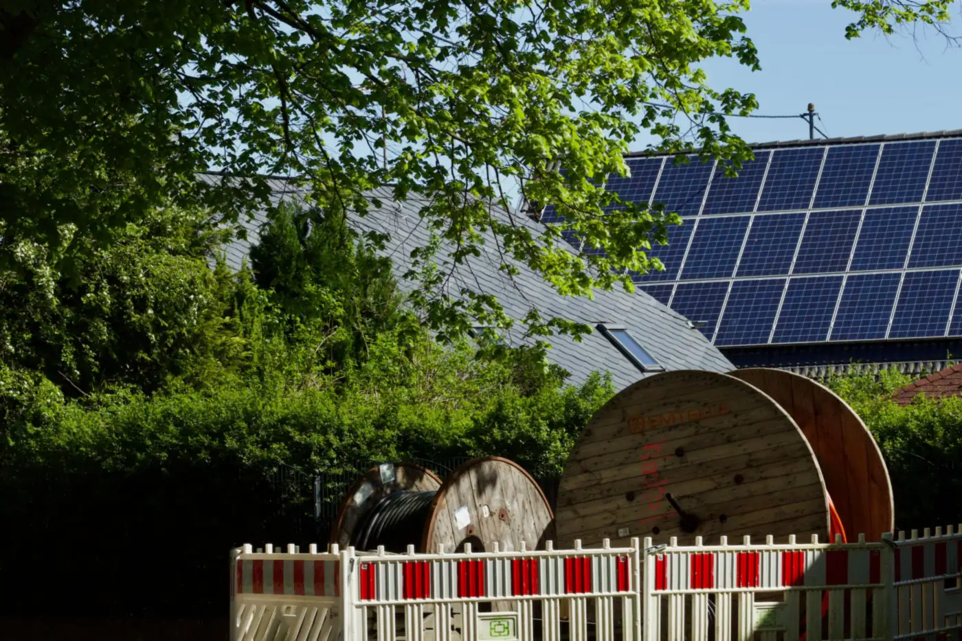 Bruchsteinhaus mit Solaranlage auf dem Dach, davor Kabeltrommeln hinter einem Bauzaun (Stadtprozelten, Landkreis Miltenberg)